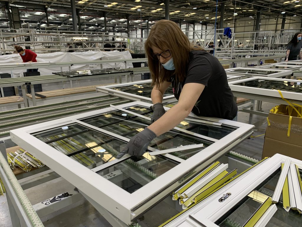 A woman engaged in the process of window manufacturing within a factory, highlighting her skill and dedication to her work.