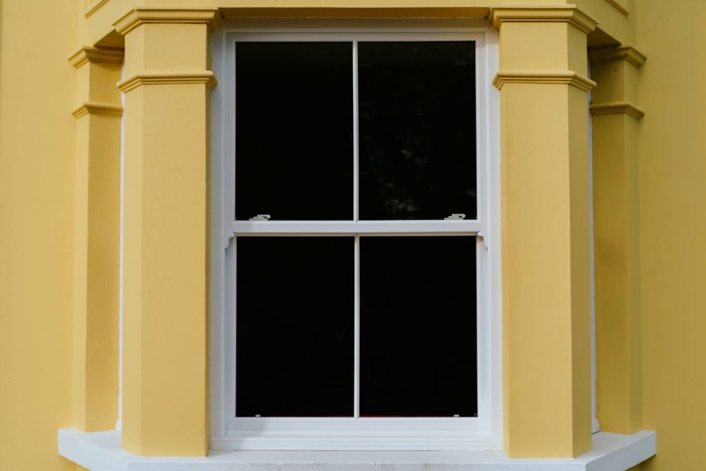 A yellow house featuring a white-framed window, showcasing a bright and cheerful exterior. 